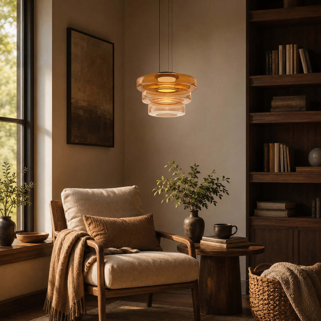 Orange three-layer glass pendant light creating a warm glow beside a reading chair and bookcase