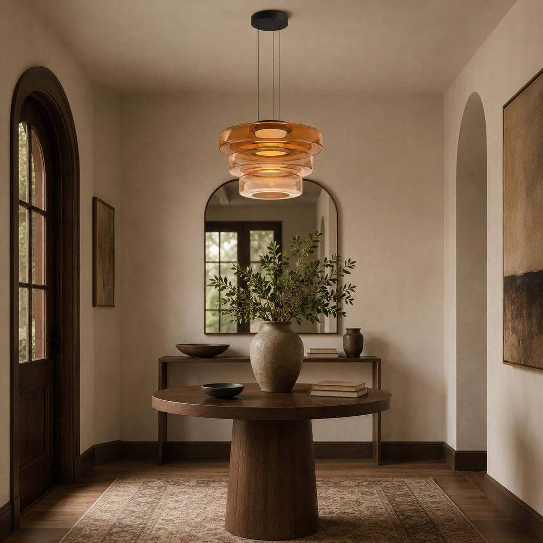 Orange three-layer glass pendant light above a round entryway table in a warm modern foyer