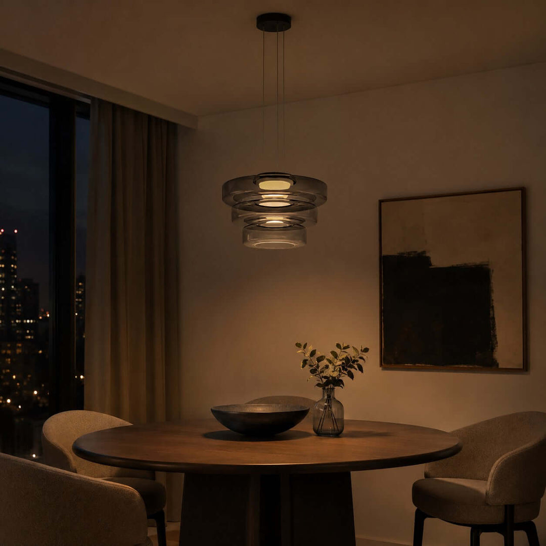 Smoke Grey three-layer glass pendant light glowing warmly above a dining table at night