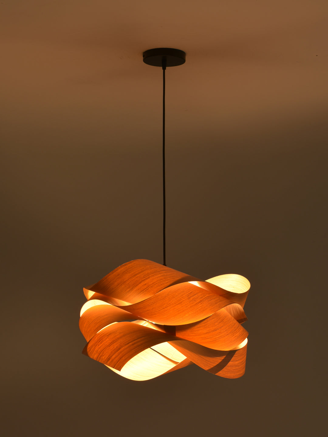Glowing Link wood pendant light suspended against a dark warm-toned background