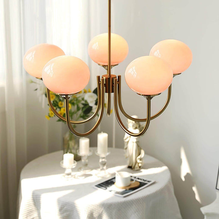 Close-up of the five-light pink glass chandelier glowing warmly above a small table.
