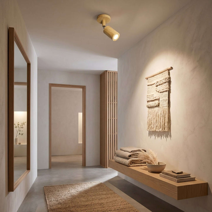 Single-head Merlo natural wood spotlight lighting a hallway wall with a woven hanging and floating wood bench