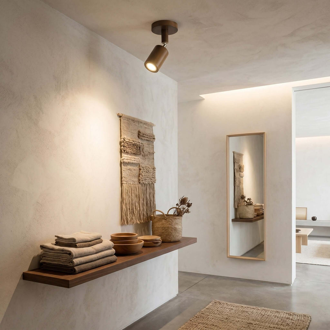 Single-head Merlo walnut wood spotlight illuminating a textured wall above an entryway storage shelf