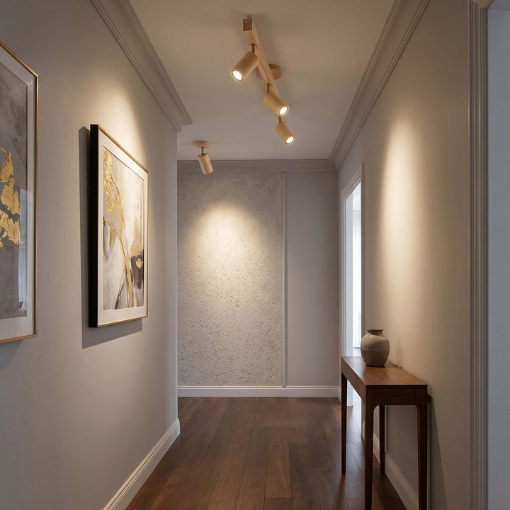 Three-head Merlo natural wood track lighting casting adjustable light along a hallway with framed artwork