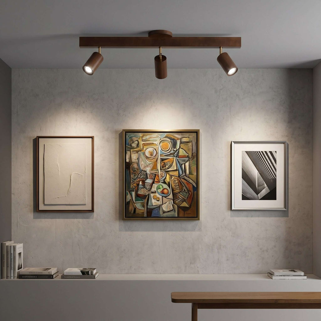 Three-head Merlo walnut track lighting illuminating a gallery wall with three framed artworks