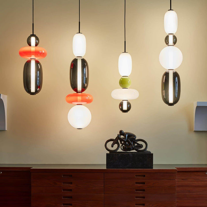 Four illuminated modern colorful glass pendant light designs above a wood console