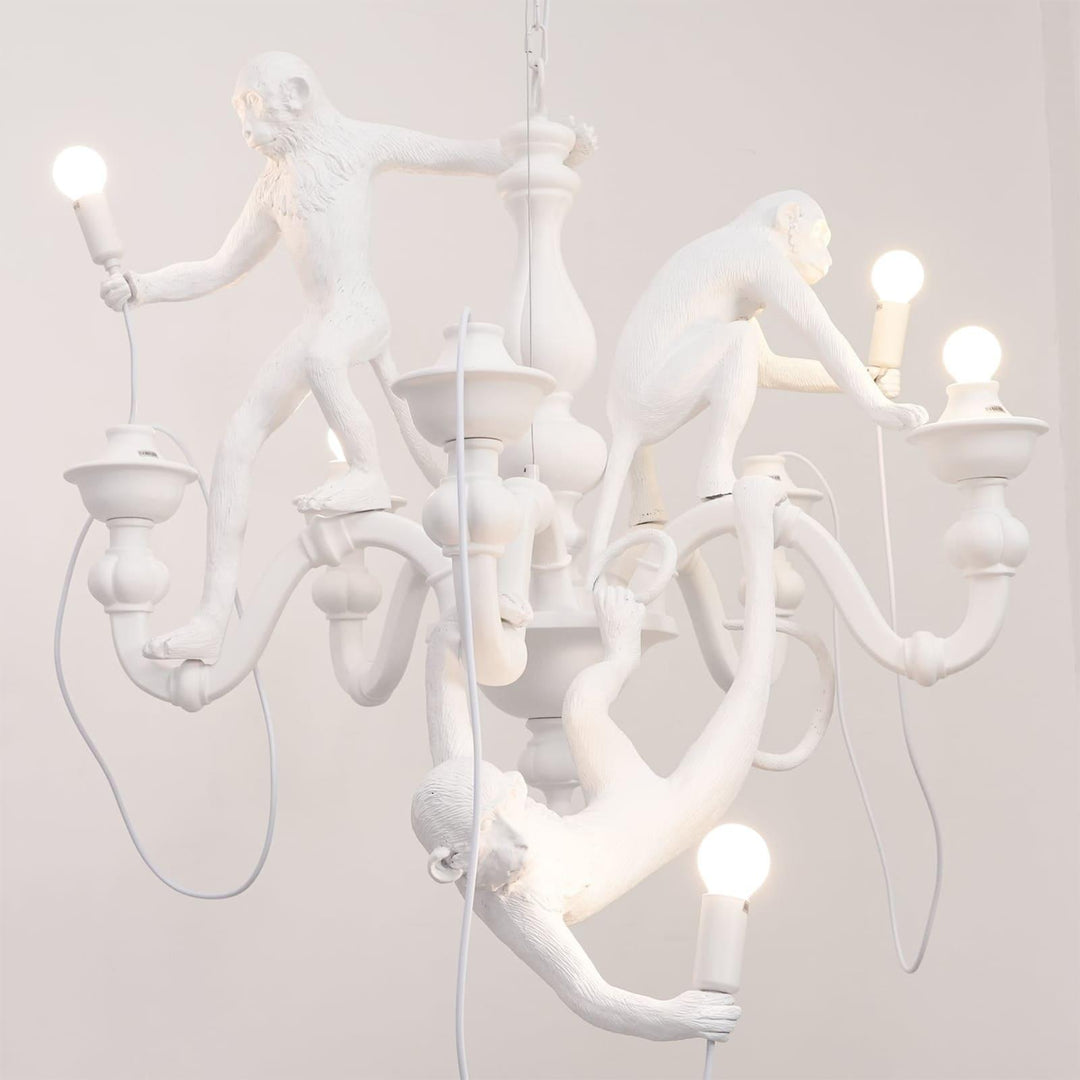 Close front view of the white three-monkey chandelier with illuminated globe bulbs