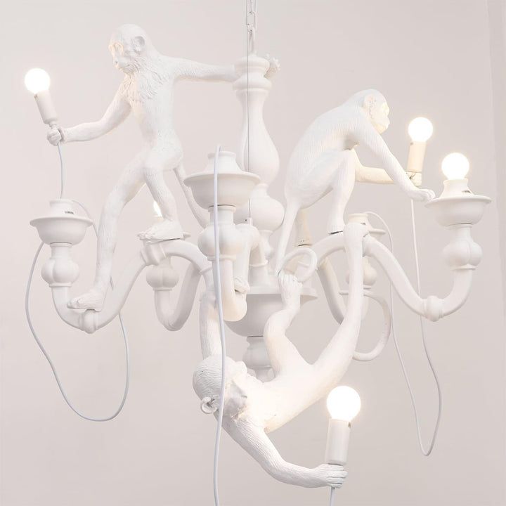 Close front view of the white three-monkey chandelier with illuminated globe bulbs