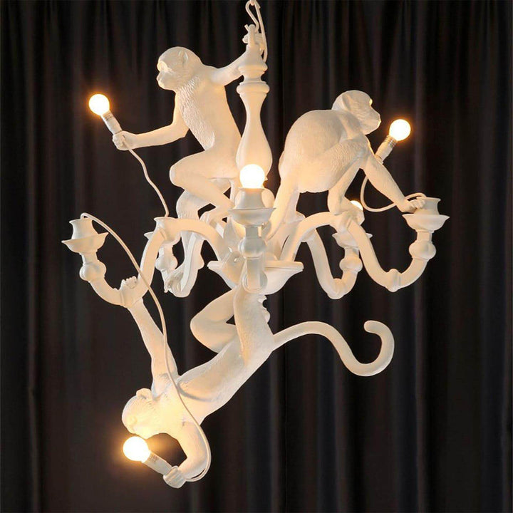 Illuminated white Monkey Chandelier with three playful resin monkeys against a black curtain