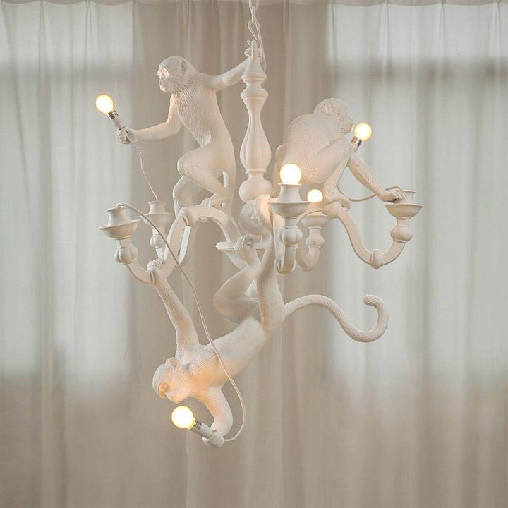Illuminated white Monkey Chandelier with three monkeys and exposed bulbs against sheer curtains