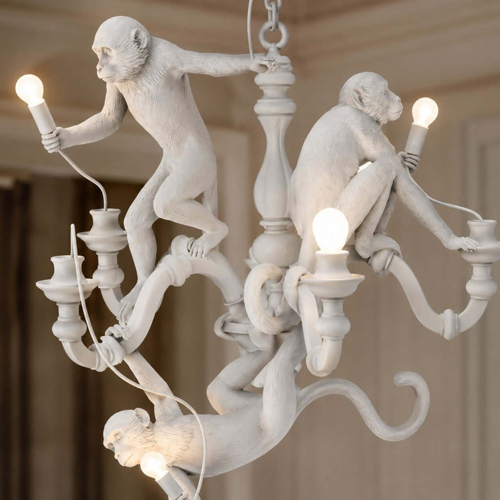 Close-up of two sculpted white monkeys holding glowing bulbs on the Monkey Chandelier