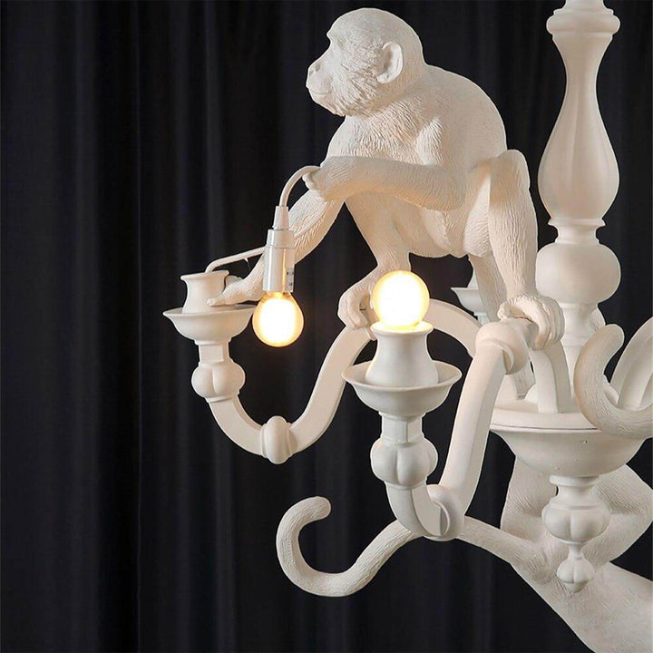 Close-up of a seated white monkey holding a bulb above curved chandelier arms