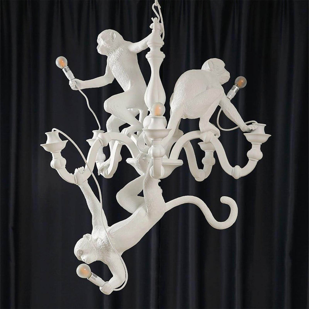 Unlit white Monkey Chandelier showing the three monkey sculptures against a black curtain