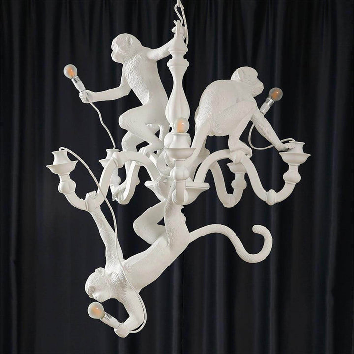 Unlit white Monkey Chandelier showing the three monkey sculptures against a black curtain
