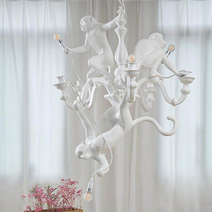 Unlit white Monkey Chandelier with three sculpted resin monkeys against sheer curtains