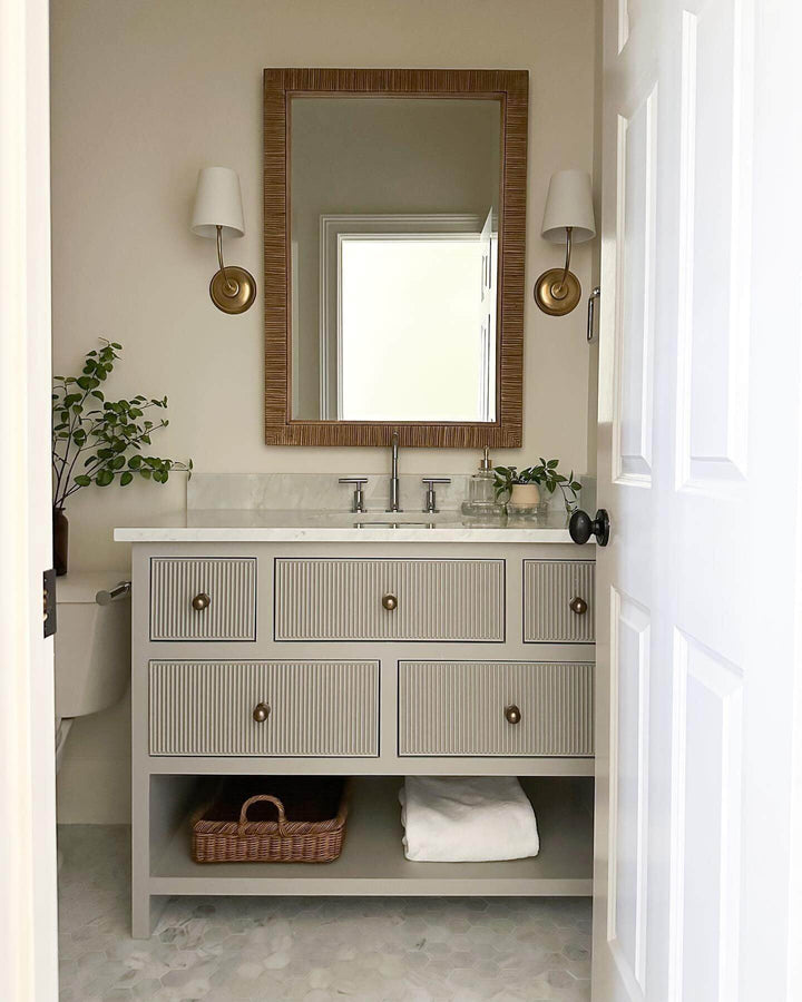 Pair of brass wall sconces beside a mirror and fluted bathroom vanity