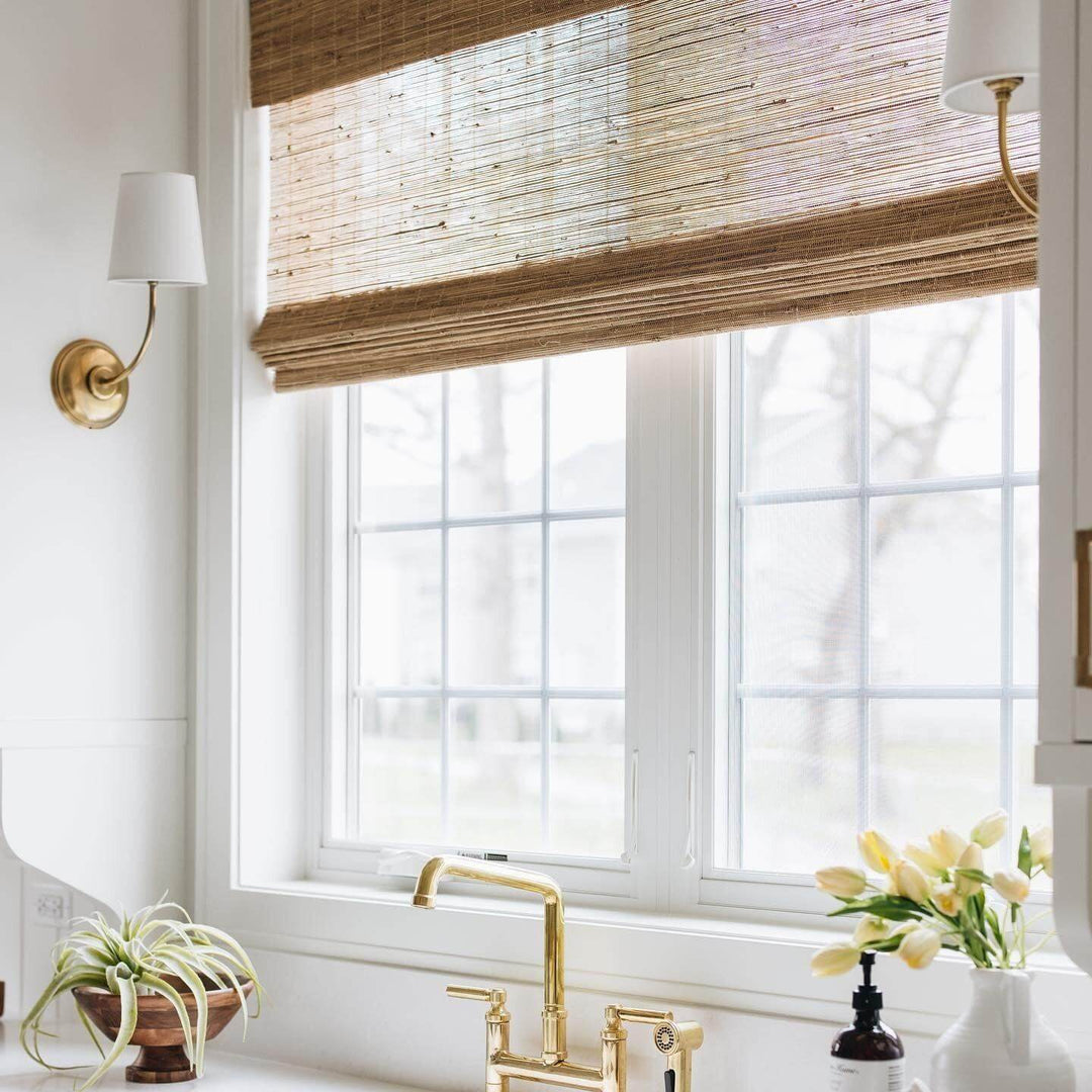 Brass single-light wall sconces framing a sunlit window above the sink