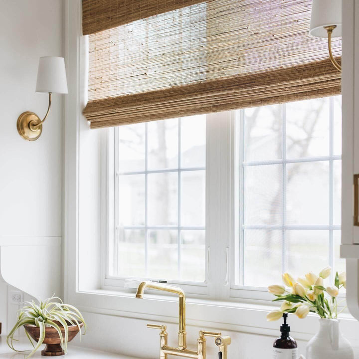 Brass single-light wall sconces framing a sunlit window above the sink