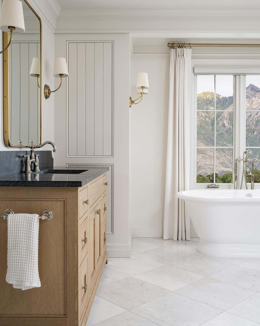 Brass wall sconces illuminating a spacious bathroom with a freestanding tub