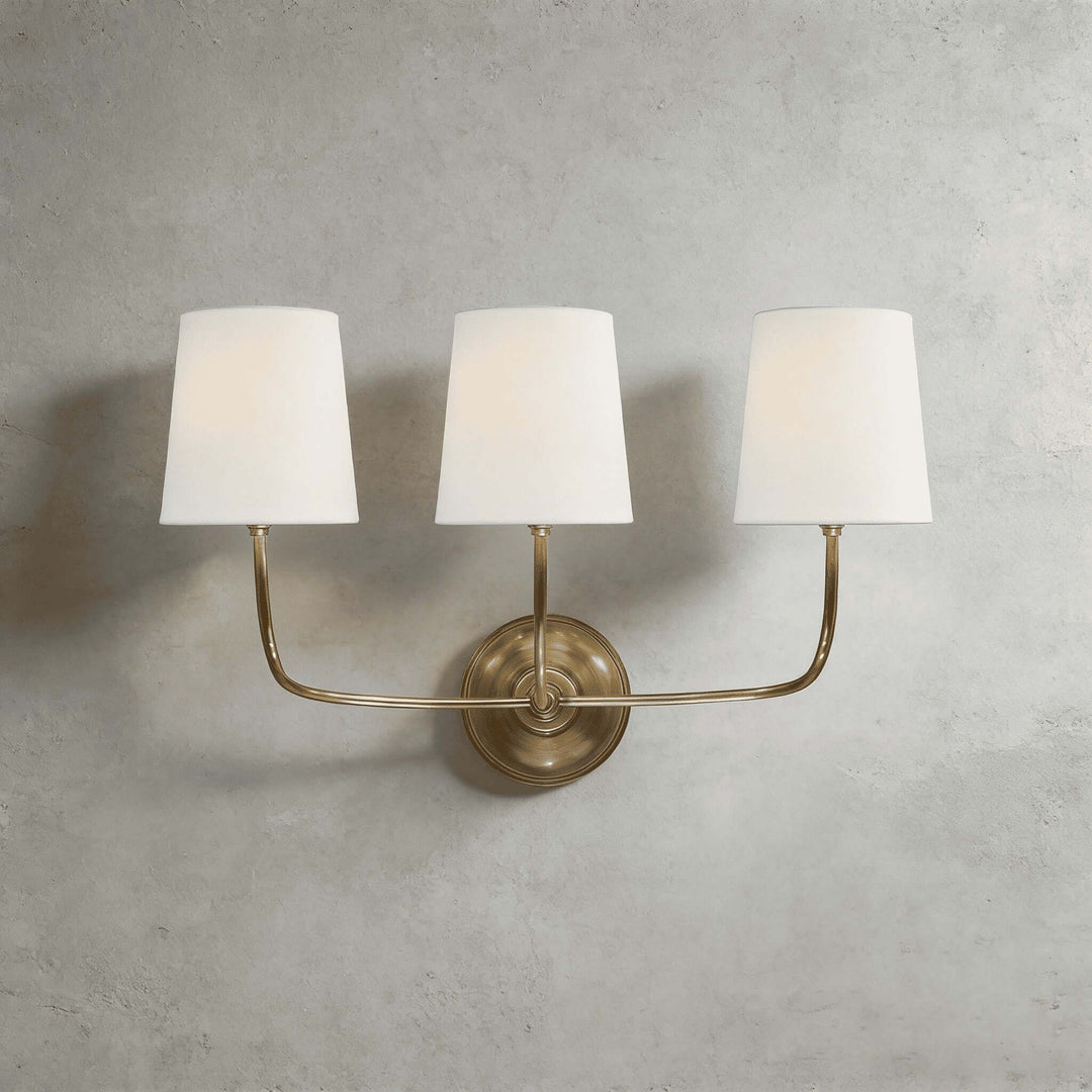 Brass three-light Multi Wall Sconce with white fabric shades on a gray wall