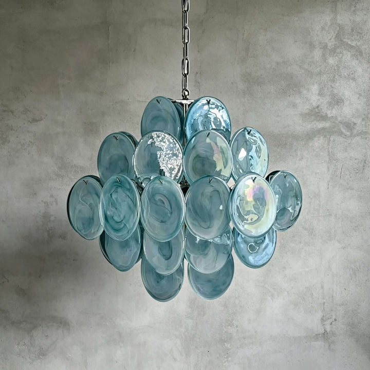 Blue Murano glass chandelier with layered translucent discs displayed against a concrete wall