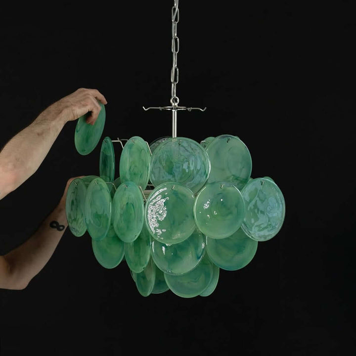 Hand attaching a green glass disc to the polished metal frame of the Murano Disk Chandelier