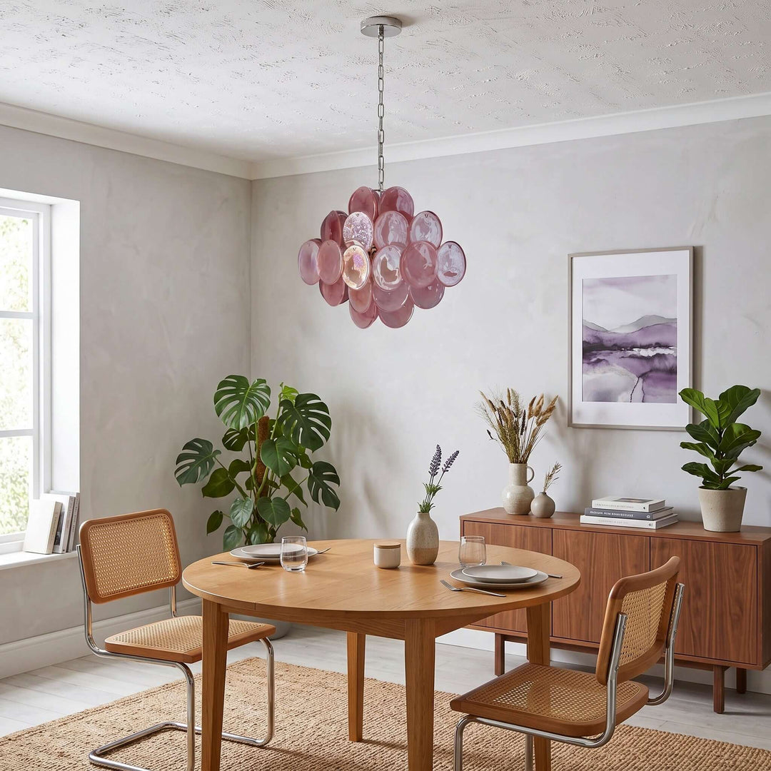 Pink Murano glass chandelier above a round dining table with cane chairs and a walnut sideboard