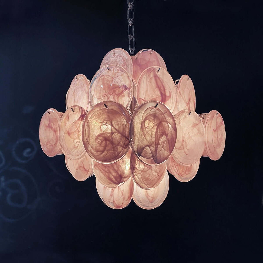 Illuminated pink Murano glass chandelier with swirling disc patterns against a dark blue background