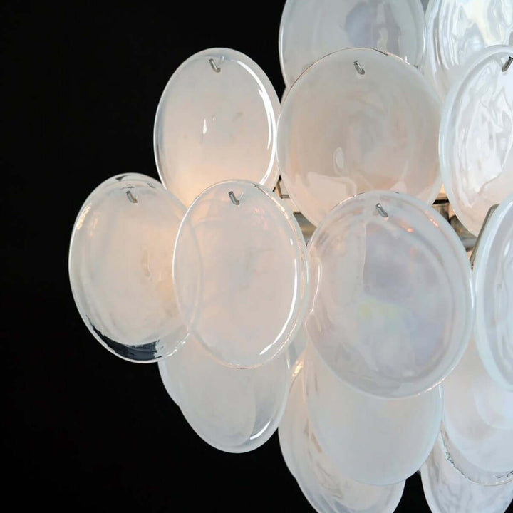 Close-up of layered white Murano glass discs with iridescent surfaces and small metal mounting hooks