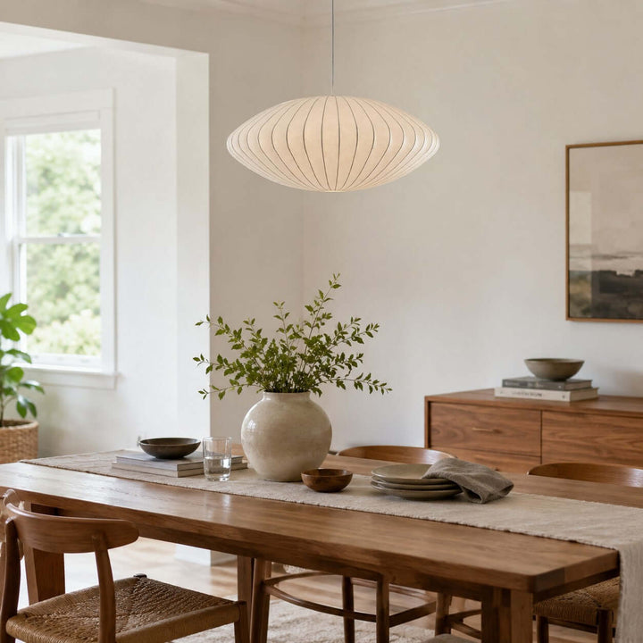White saucer-shaped Nelson Bubble pendant light above a wood dining table in a bright minimalist dining room
