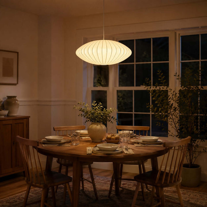Glowing saucer Nelson Bubble pendant lamp above a round dining table in a warmly lit evening interior