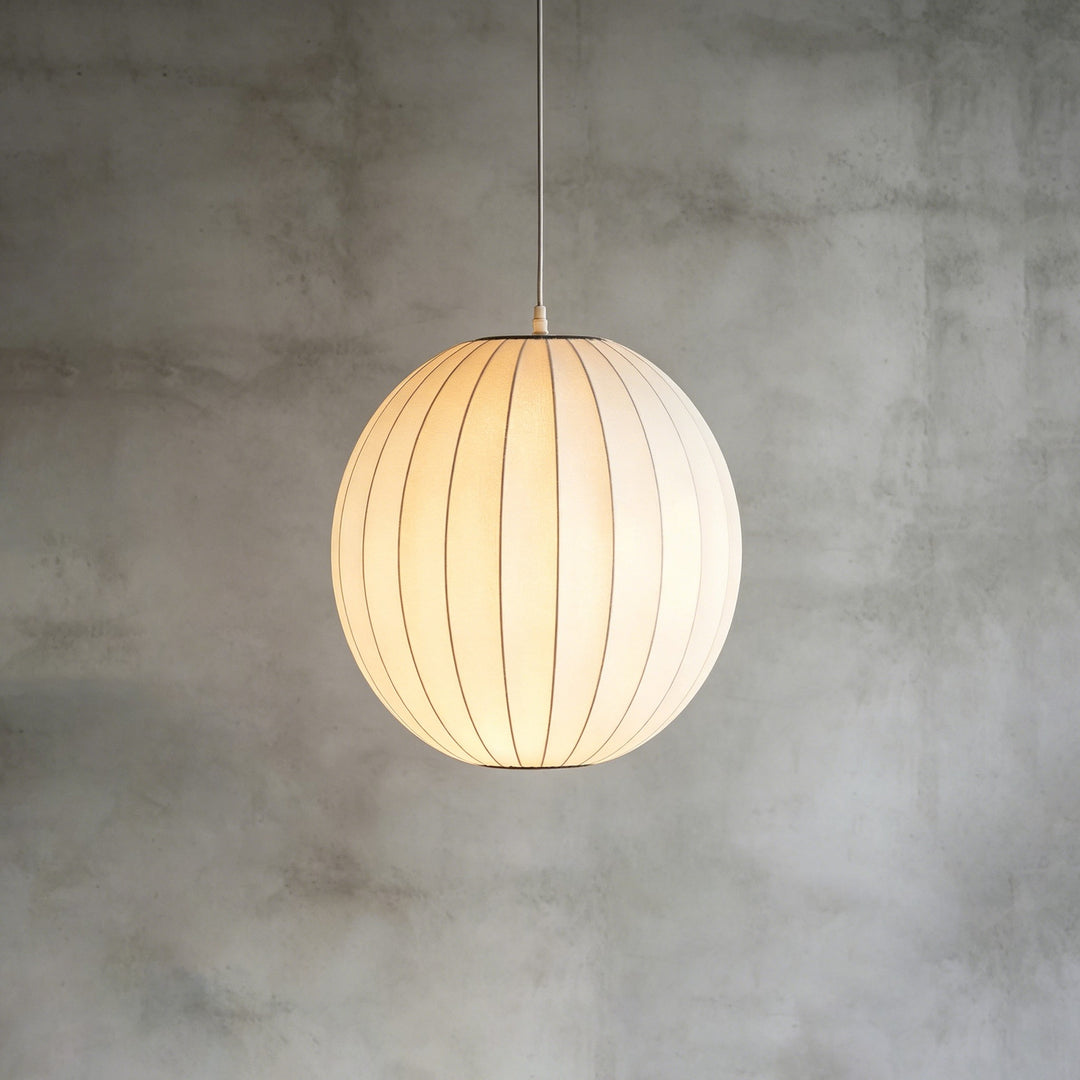 Globe-shaped Nelson Bubble pendant light with a softly glowing white silk shade on a concrete backdrop