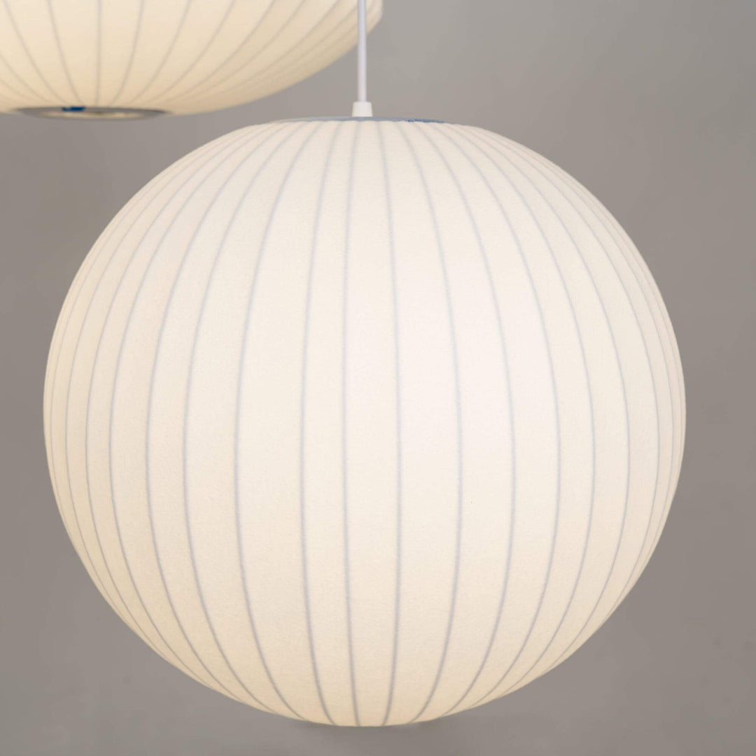 Glowing globe-shaped Nelson Bubble pendant lamp with a white ribbed silk shade on a gray background