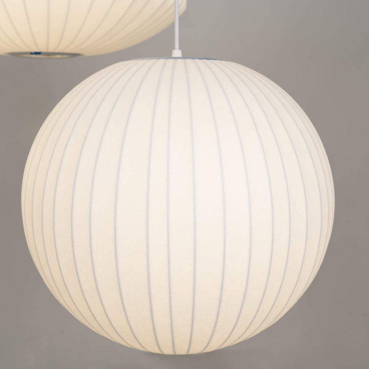 Glowing globe-shaped Nelson Bubble pendant lamp with a white ribbed silk shade on a gray background