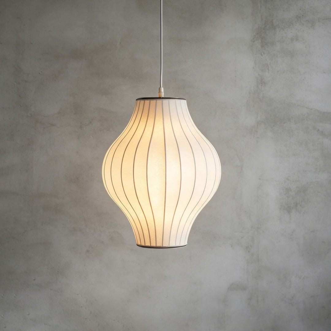 Hourglass-shaped Nelson Bubble pendant lamp with a glowing white silk shade against a concrete backdrop