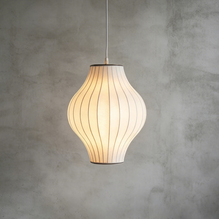 Hourglass-shaped Nelson Bubble pendant lamp with a glowing white silk shade against a concrete backdrop