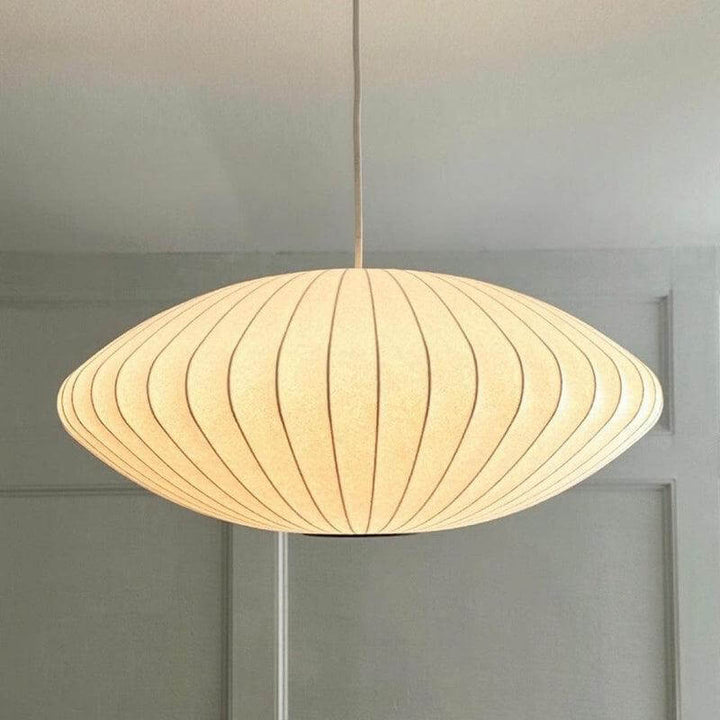 Close view of a glowing Nelson Bubble saucer pendant light against a paneled neutral wall
