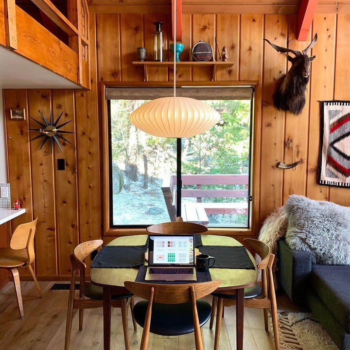 Glowing Nelson Bubble saucer pendant light above a dining and work table in a rustic wood-paneled cabin