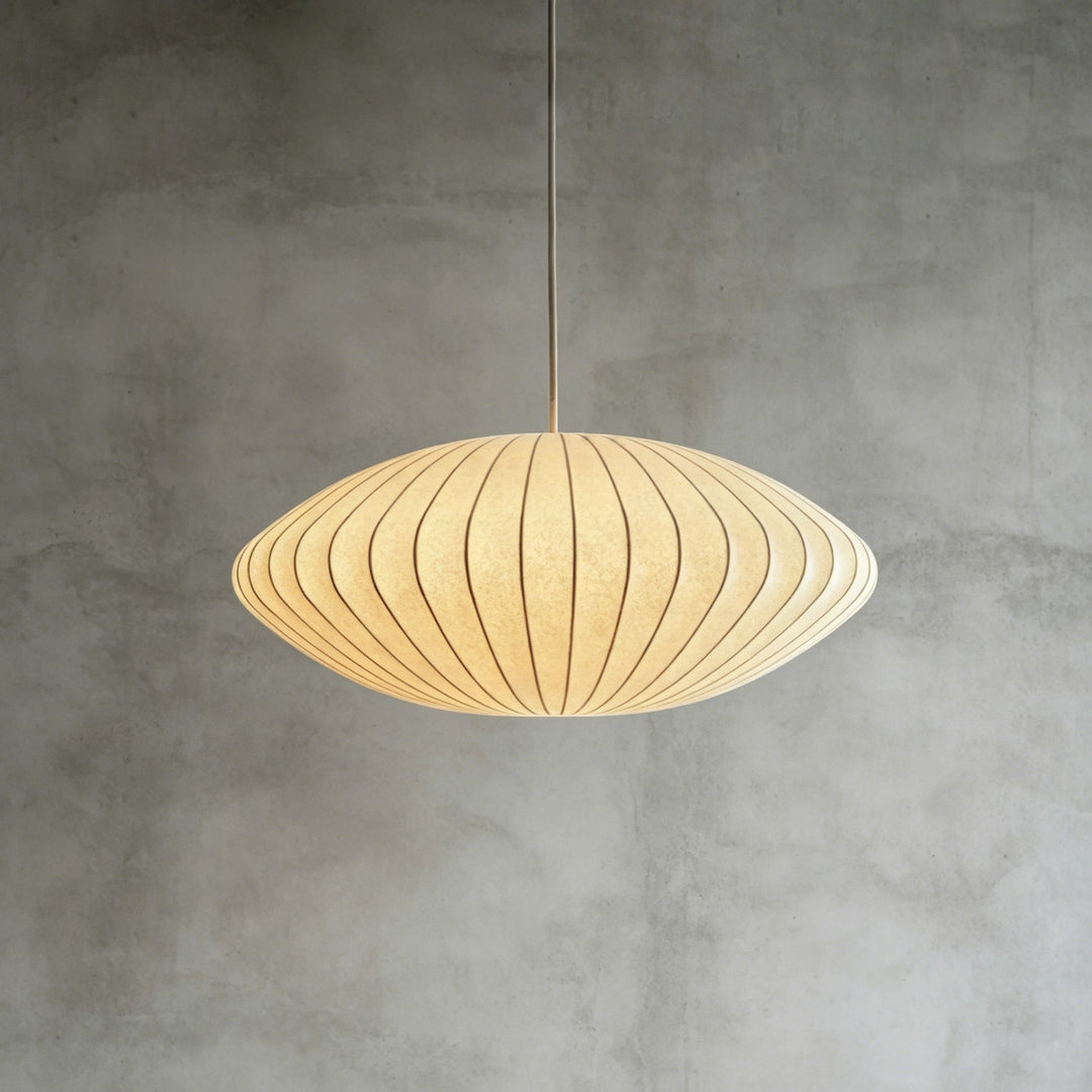 Saucer-shaped Nelson Bubble pendant lamp glowing warmly against a textured concrete background