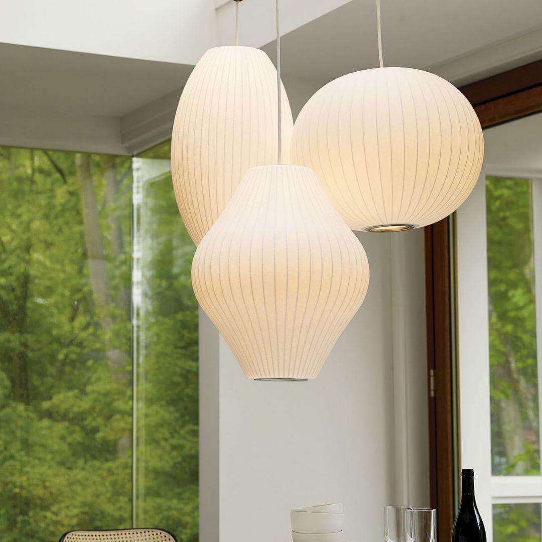 Cluster of three glowing Nelson Bubble pendant lights in globe, oval and hourglass shapes beside large windows