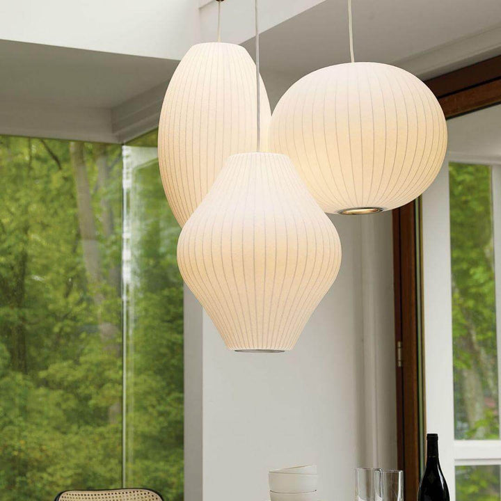 Cluster of three glowing Nelson Bubble pendant lights in globe, oval and hourglass shapes beside large windows