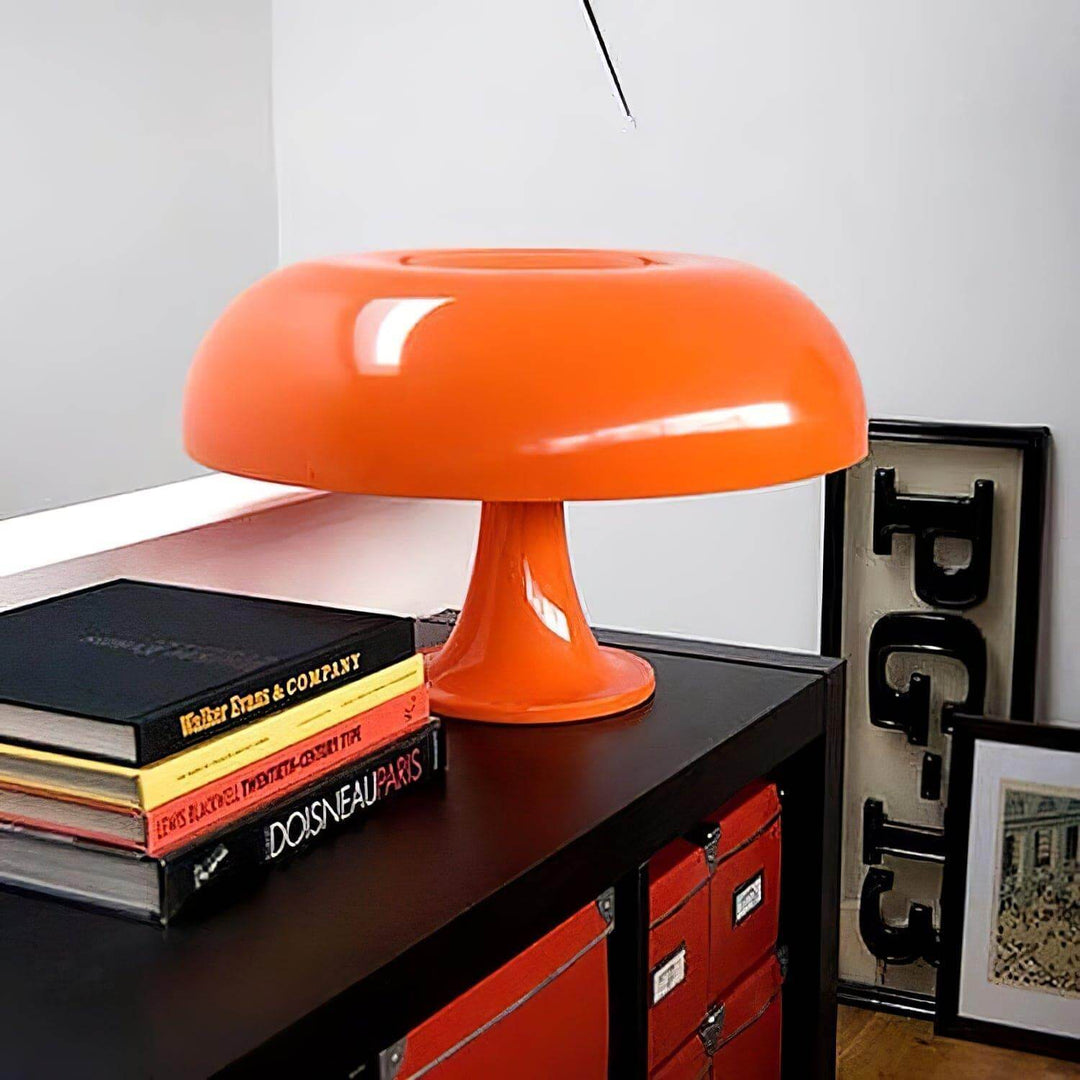 Orange Nesso Table Lamp on a black cabinet surrounded by books and framed art