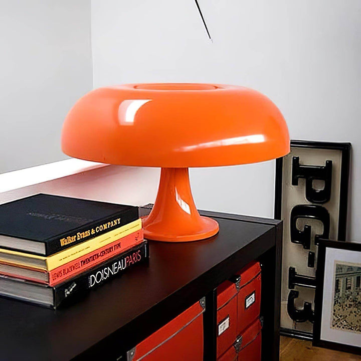Orange Nesso Table Lamp on a black cabinet surrounded by books and framed art