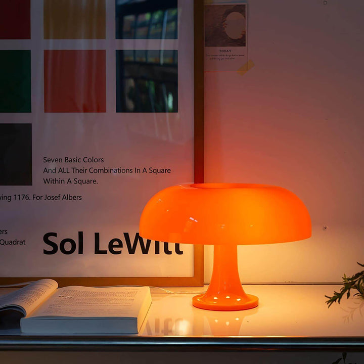 Glowing orange Nesso Table Lamp beside an open book and graphic wall art