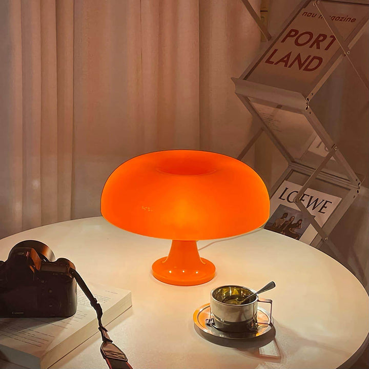 Glowing orange Nesso Table Lamp on a round table with a camera and coffee cup
