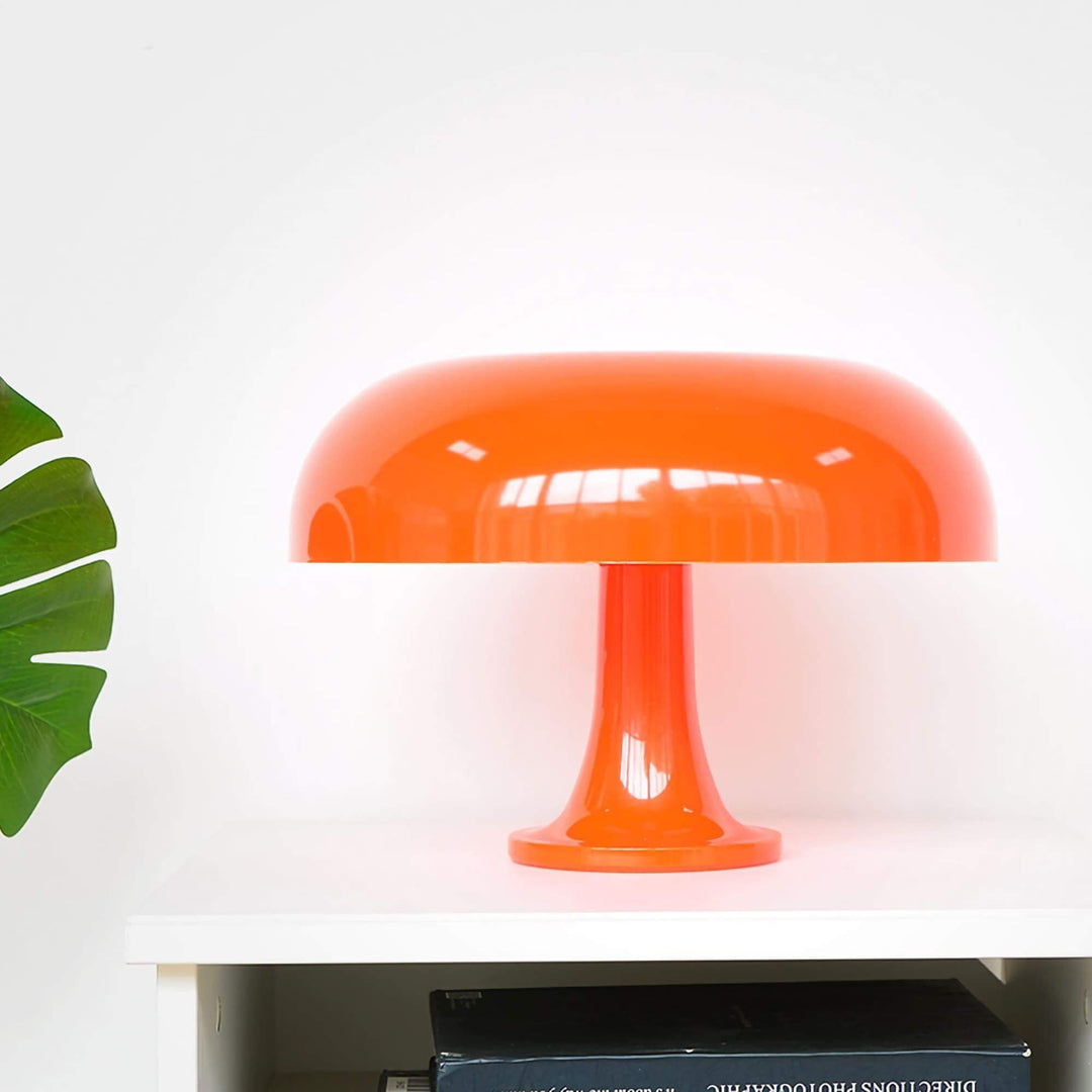 Orange Nesso Table Lamp displayed on a white shelf beside a green plant