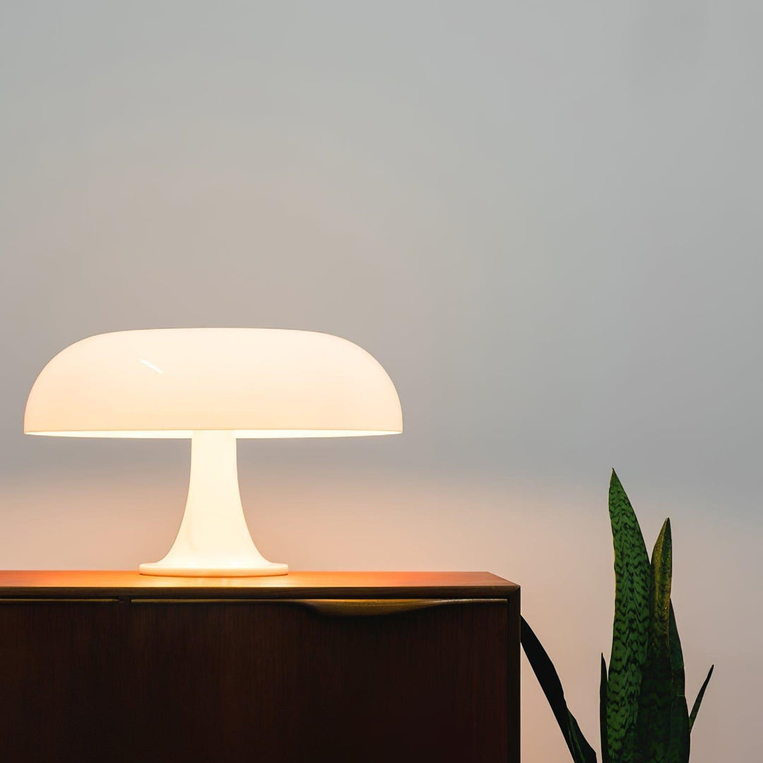 Glowing white Nesso Table Lamp on a dark wood console beside a snake plant