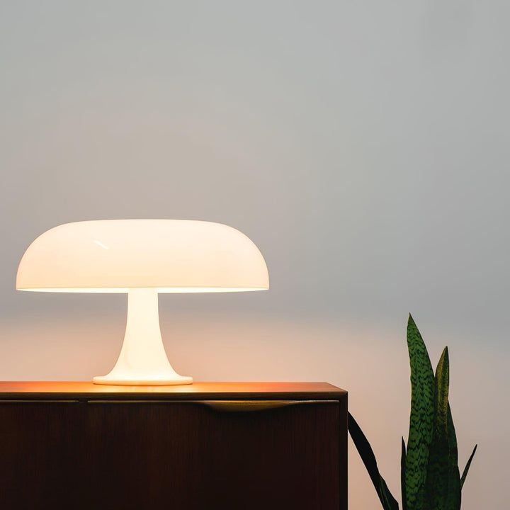 Glowing white Nesso Table Lamp on a dark wood console beside a snake plant