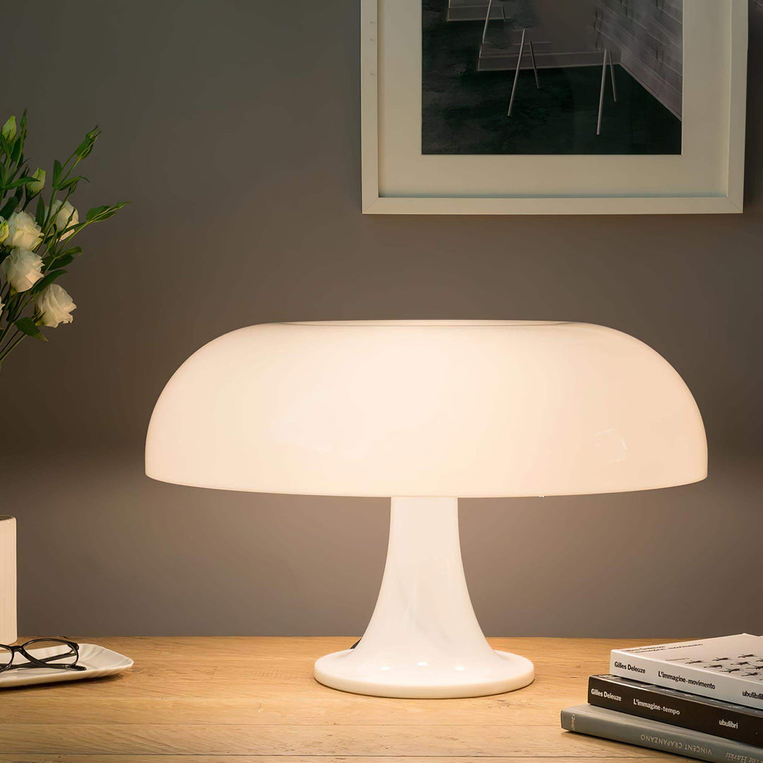 Glowing white Nesso Table Lamp on a wood desk with books and flowers