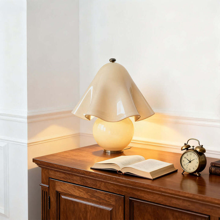 Amber glass table lamp illuminating a wood sideboard beside an open book and alarm clock